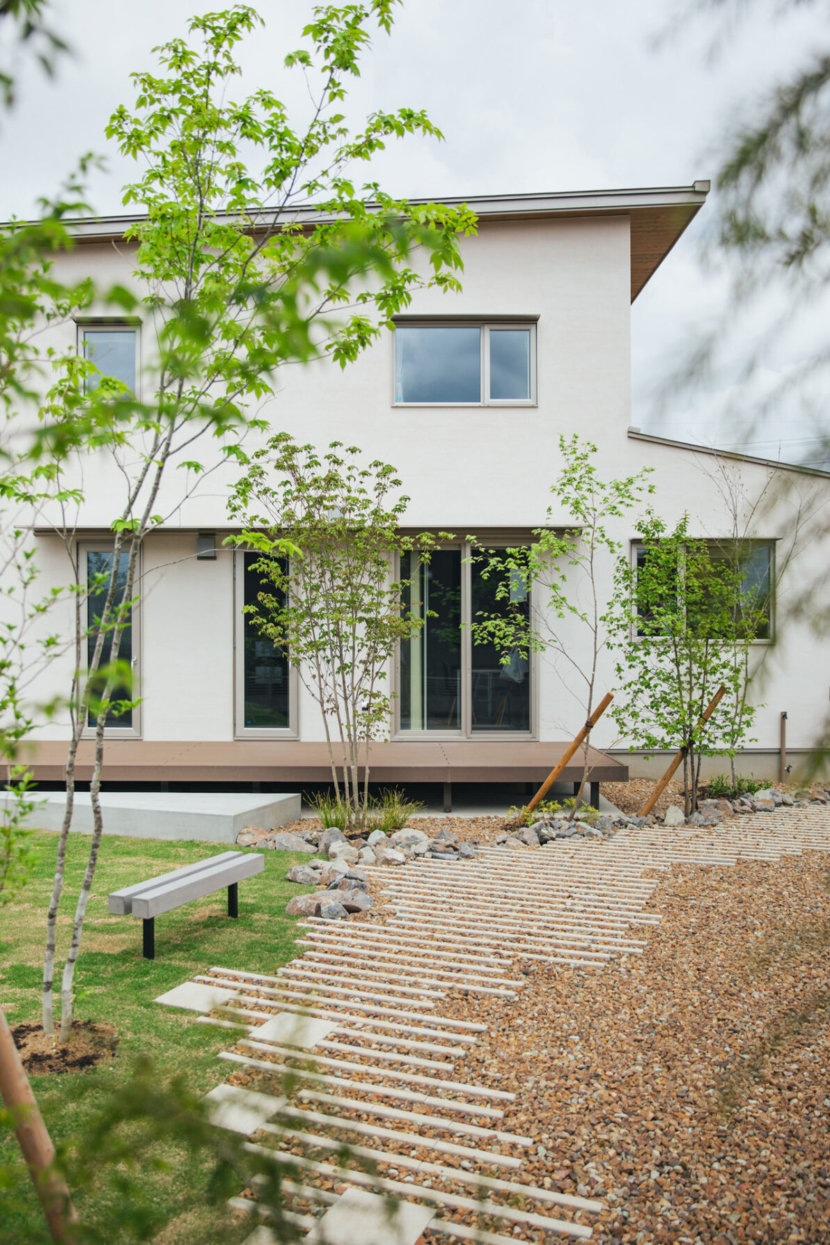 植栽越しに見る、庭とデッキが連続する住宅外観